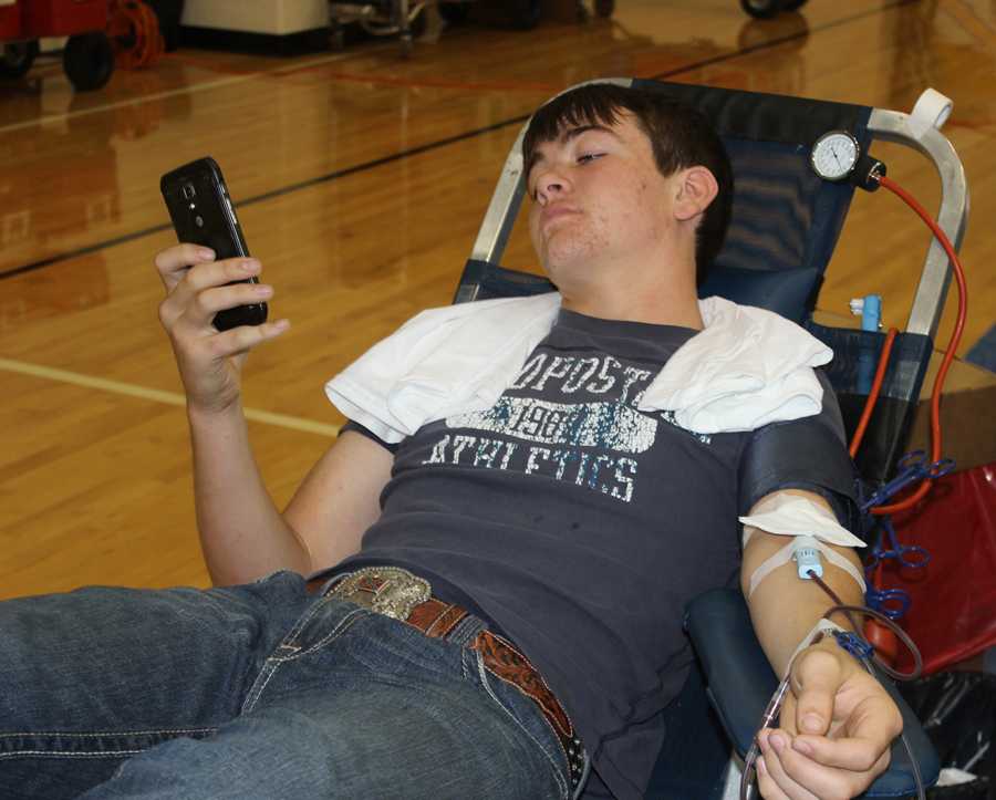 Junior Trey Minter relaxes with his cell phone while donating blood Friday. The NHS-sponsored events collected 69 units for donation.