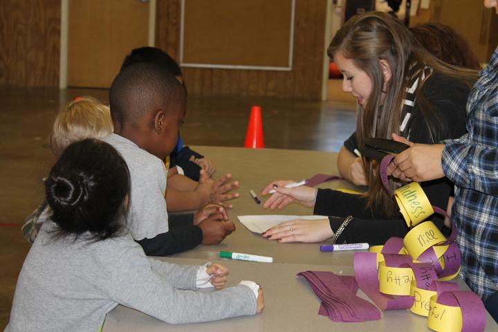 Senior Haylee Brewer helps elementary students write kind words for a chain of kindness at an FCCLA bullying activity. The event is part of a bullying prevention project.