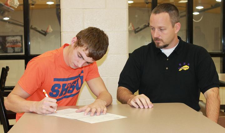 Senior Tyler Adams signs his letter of intent with Sam Houston State University, where he will run track next year, while coach Clay Hodges looks on. Tylers scholarship will total up to about three-quarters of his college expenses.