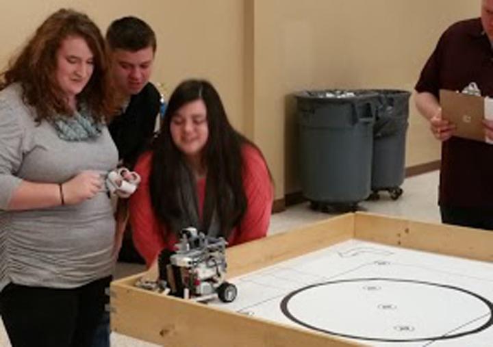 Robotics+members+Brittany+Scott%2C+Cody+Pilkington+and+Kaiden+Loep+watch+nervously+as+their+robot+runs+the+course+at+area+competition.+