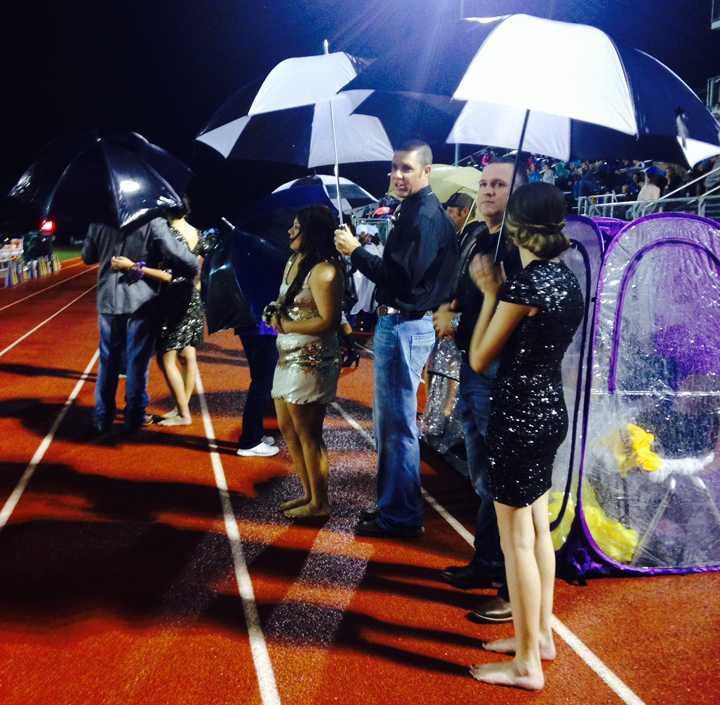 The homecoming queen candidates and their escorts use umbrellas to try to stay dry as they wait for halftime to start.