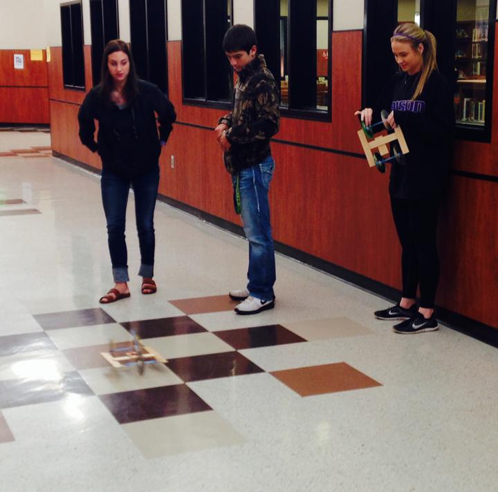 Physics students Gracie Ferguson and Hannah Eakin practice with their mouse trap cars while classmate Shelley Pate watches.