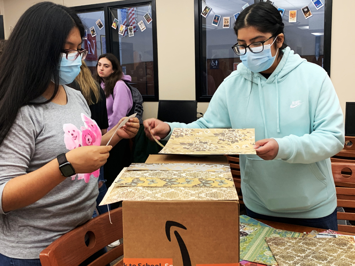 Student council members cover recycled boxes with scrapbook paper so that teachers can have decorated boxes to collect paper in for recycling. 