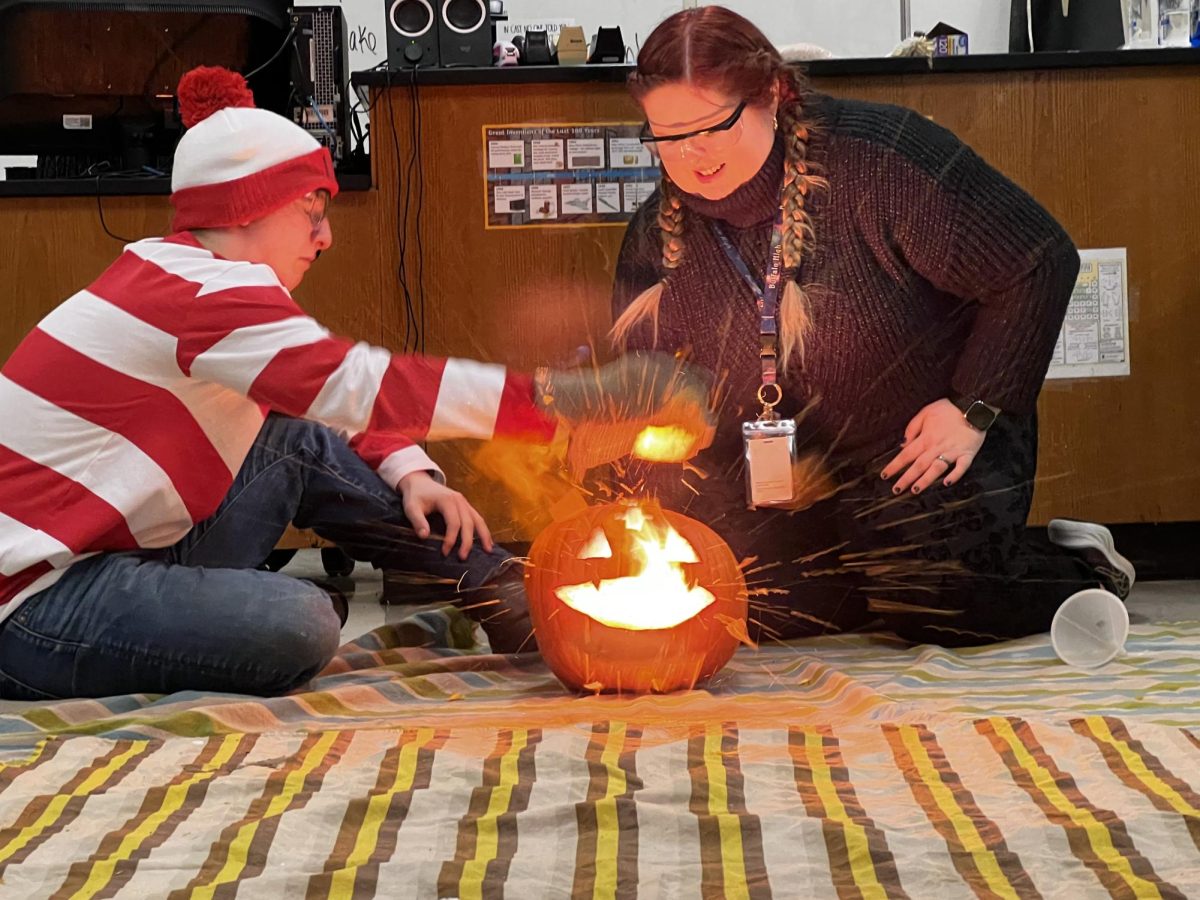 Rex Webb and teacher Kristine Lenamond light one of the pumpkins during their class experiment. 